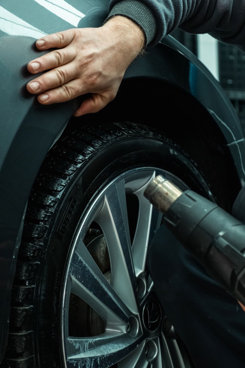 Main d'un mécanicien posée sur l'aile d'une voiture, roue et visseuse au premier plan